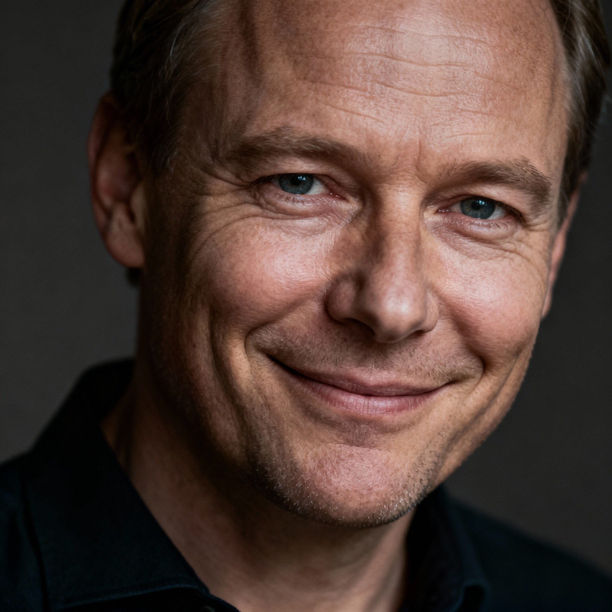 A close-up portrait of a male psychic in his 40s with a gentle, knowing smile. His eyes are wise and empathetic, and the soft lighting highlights his trustworthy and professional demeanor.